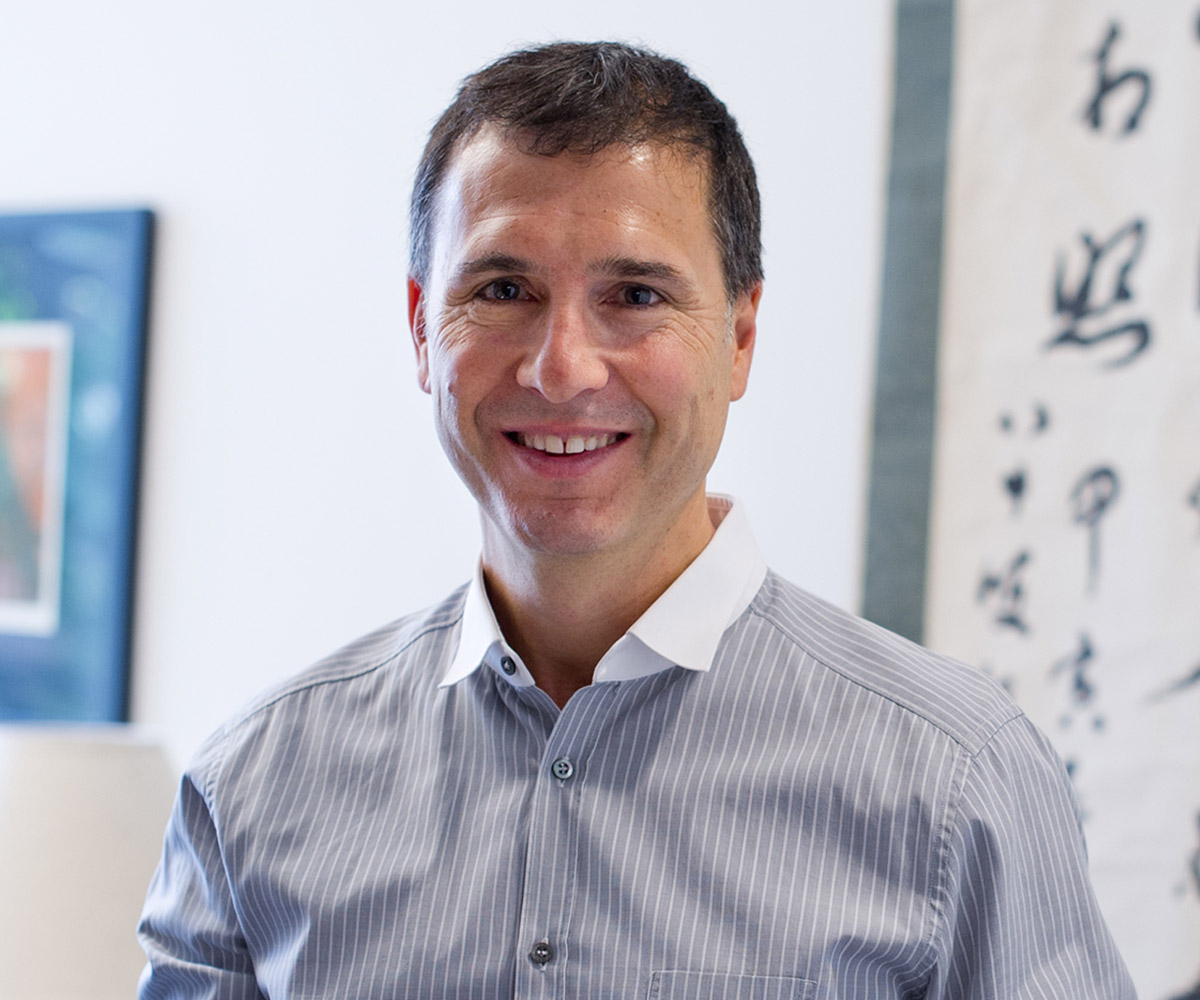Eric A. Feldman Eric A. Feldman smiling while wearing a gray buttoned down shirt